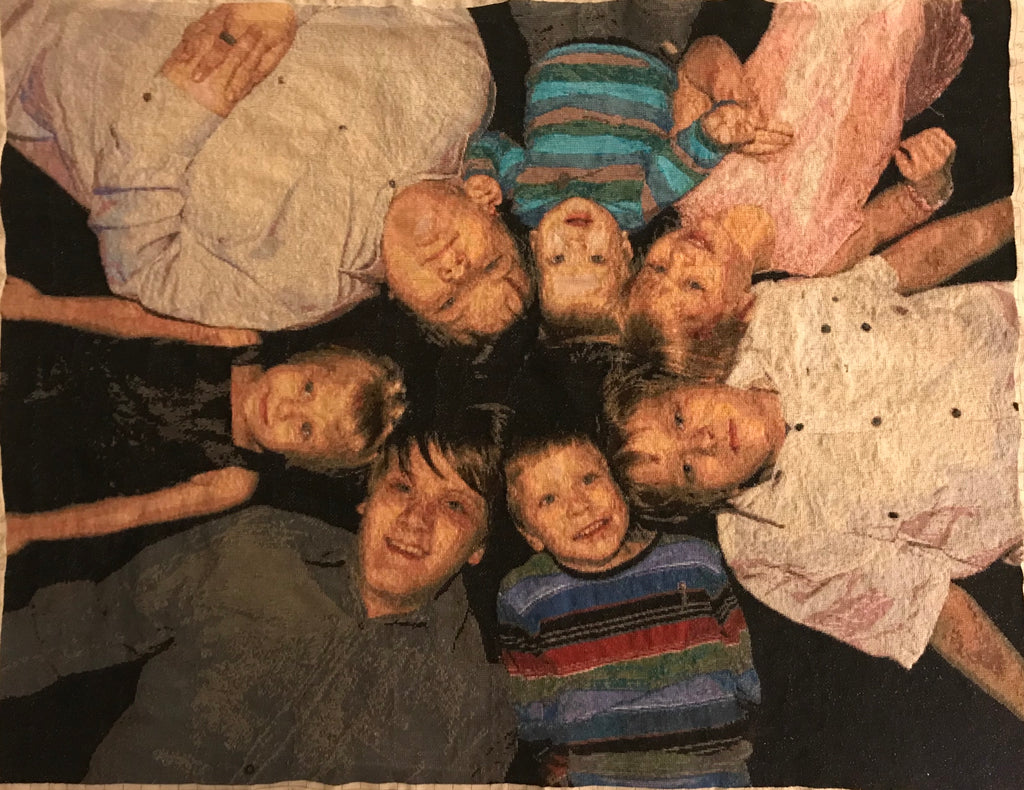 Family photo of our 7 children stitched in 18ct. A family moment in stitches: children in a circle, heads together, dark background